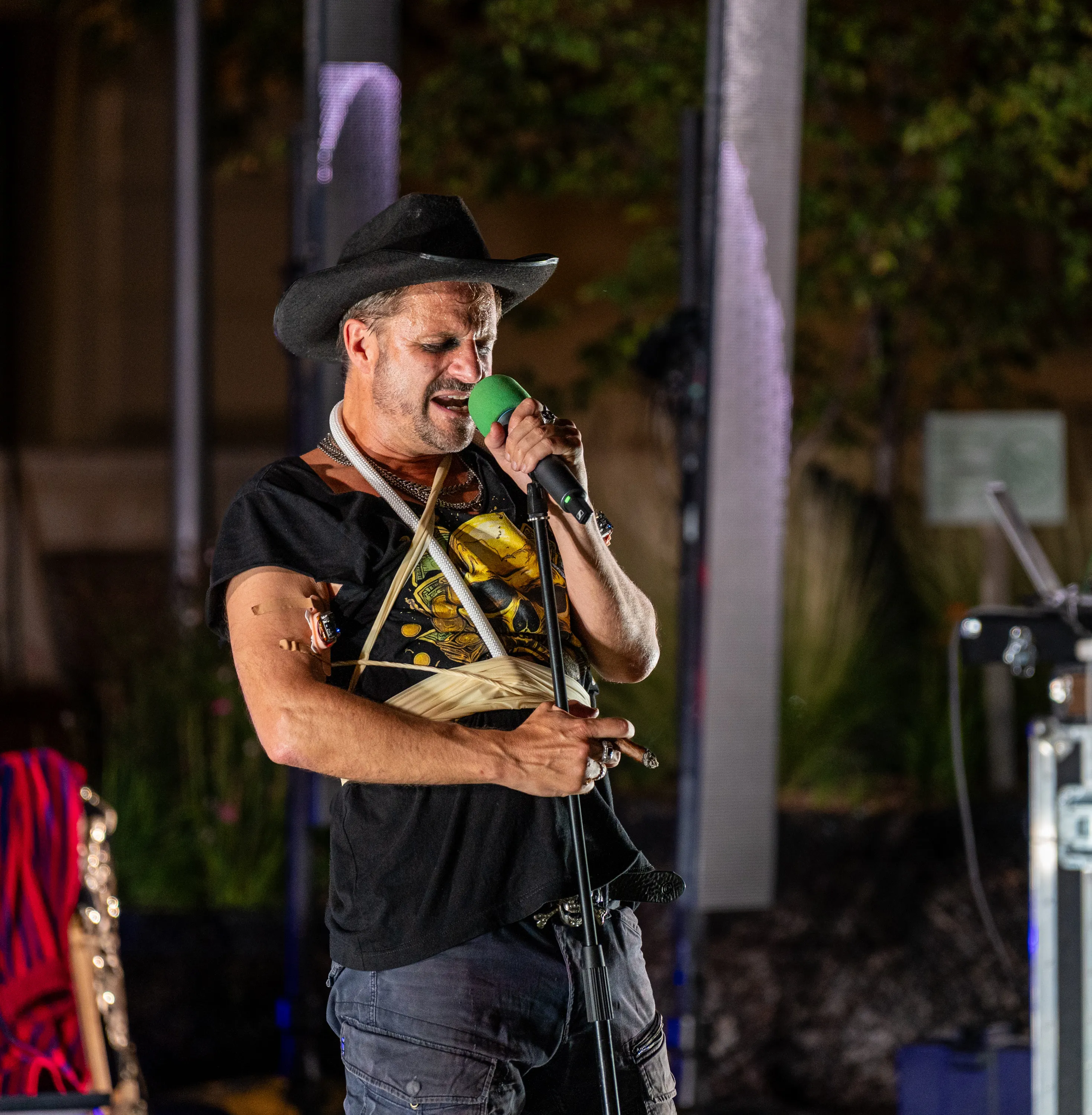 Philipp Hochmair performing at Vienna’s MuseumsQuartier, wearing a black hat and T-shirt, with his eyes closed and a green-topped microphone held close to his mouth.